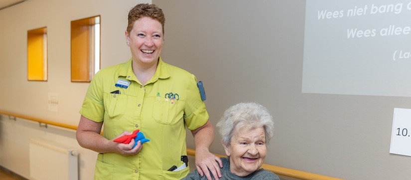 Mevrouw in rolstoel staat met medewerker Revalidatie in gang en lachen