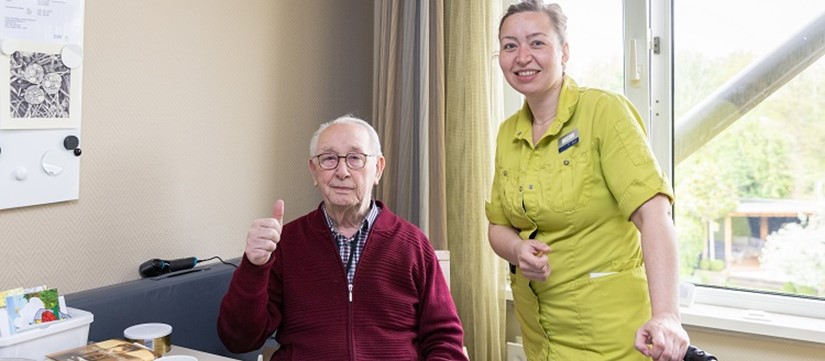 Meneer zit achter tafel en steekt duim op met naast hem medewerker Revalidatie